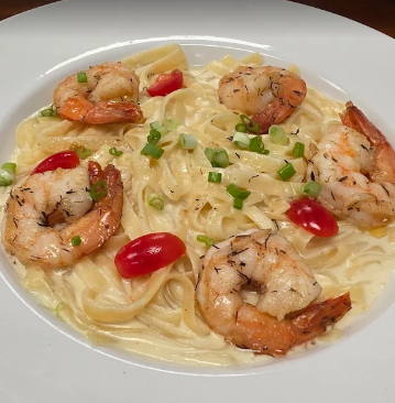 Garlic shrimp pasta with cherry tomatoes and green onions on a white plate